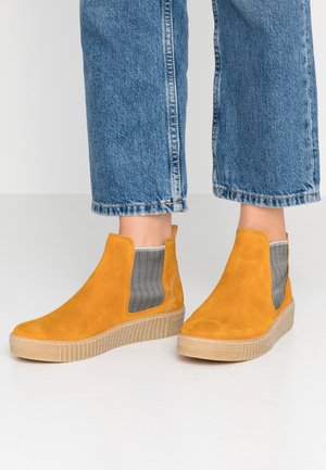 Bottines en daim jaune avec des panneaux latéraux élastiques et une semelle beige texturée, présentant un design élégant avec un bout arrondi et un minimum de détails.