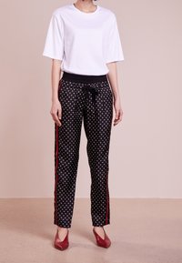 Vit kortärmad t-shirt som matchas med svarta mönstrade byxor med dragsko i midjan, röda sidostenar och cirkulära vita mönster.