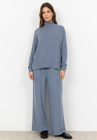 Light blue, loose-fitting loungewear set featuring a high-neck top and wide-leg pants, made of soft, textured fabric. Black shoes complete the look.