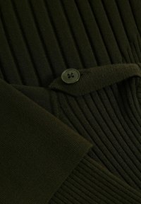 Dunkelgrüner gerippter Stoff mit einem strukturierten Muster, einem runden grünen Knopf und einem gefalteten Abschnitt. Weiche Textur und strukturiertes Design.