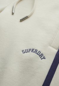 Crème hoodie van een katoenmix; heeft marineblauwe accenten, geborduurd "SUPERDAY" in een boog. Inclusief een capuchon met trekkoord en een geribde zoom.