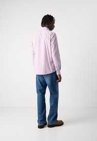 Camisa de manga larga a rayas en rosa claro y blanco, de tela ligera, con cuello clásico, combinada con jeans de denim azul y calzado marrón.