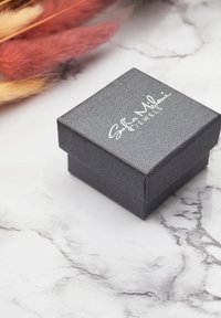 Svart texturerad smyckeslåda med ett gångjärnslock, med vittryckt text "Sophie Milani Jewels" på toppen. Ligger på en marmorbakgrund.