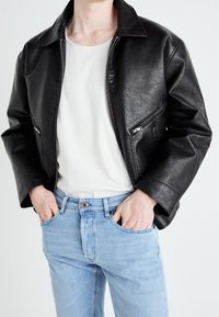 Černá bunda z umělé kůže se stříbrnými zipy, širokým límcem a volným střihem, ve spojení s světle modrými džínami a bílým tričkem.