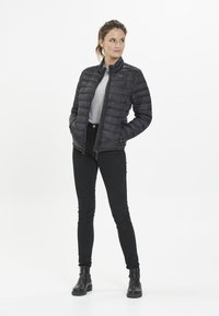Svart puffjacka med hög krage, horisontellt quiltad mönster, två framfickor, matchad med svarta skinny jeans och ankelstövlar.