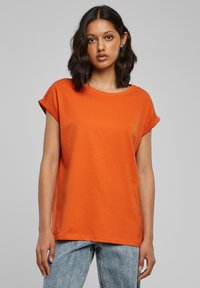 Oranje T-shirt met korte mouwen, een ronde halslijn en opgerolde manchetten, gemaakt van lichtgewicht stof. Gecombineerd met lichtblauwe spijkerbroek.