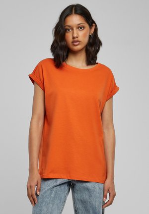 Orange t-shirt med korte ærmer, rund halsudskæring og opkrullede ærmekanter, lavet af letvægtsstof. Kombineret med lyseblå denimjeans.
