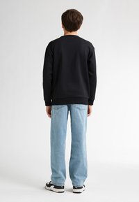Sudadera negra, corte relajado, puños acanalados. Vaqueros azul claro, corte holgado, tela desgastada. Zapatillas negras y blancas con suela distintiva.