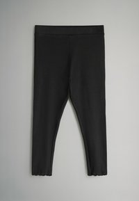 Leggings negros de tela acanalada, con un diseño ajustado, textura suave y dobladillos en forma de concha en los tobillos.