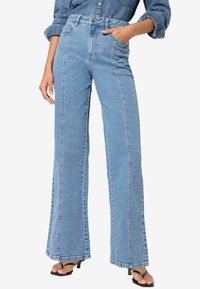 Hellblaue hochgeschnittene Bootcut-Jeans aus glattem Denim mit Fronttaschen und sichtbaren Nähten entlang der Säume.