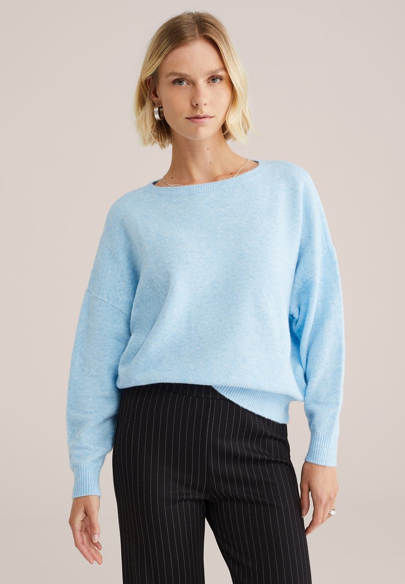 Lichtblauwe, oversized trui met een ronde hals en verlaagde schouders. Zachte textuur, geribde manchetten en een relaxte pasvorm in combinatie met gestreepte broek.