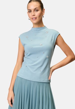 Himmelblaues, ärmelloses Oberteil mit hohem Kragen, verziert mit floralen Mustern und kleinen Edelsteinen, hergestellt aus einem weichen, strukturierten Stoff.