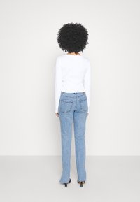 Vit långärmad tröja med rund halsringning, matchad med ljusblå raka jeans som har två bakfickor och lätt fransade fållar.