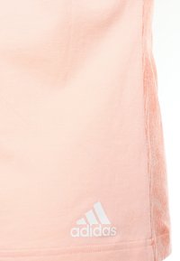 Světle růžový sportovní top vyrobený z měkké tkaniny, s texturovaným bočním panelem a bílým logem Adidas blízko lemu.