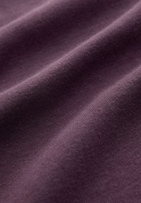 Lila Baumwollstoff mit glatter Textur und dezenten Rippen, der sanfte Falten und Knicke im natürlichen Licht zeigt.