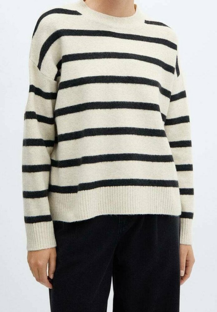 Kremowy sweter z czarnymi poziomymi paskami, okrągłym dekoltem i ribbowymi mankietami. Miękka tekstura i luźny krój, noszony z czarnymi spodniami.