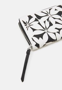 Portefeuille noir et blanc avec un design floral découpé, fabriqué en cuir avec une fermeture éclair et une languette en tissu noir.