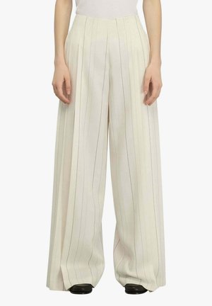 Pantaloni a gamba larga color crema con sottili righe verticali, indossati con scarpe nere e una maglietta bianca, vista frontale dalla vita ai piedi.