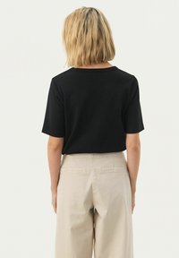 Maglietta nera a maniche corte con vestibilità rilassata, abbinata a pantaloni beige chiaro a vita alta con due tasche posteriori e una trama liscia.