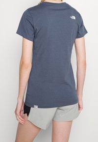 Ciemnoniebieska bawełniana koszulka z okrągłym dekoltem, krótkimi rękawami i małym logo na górnej części pleców, zestawiona z jasnoszarymi szortami.