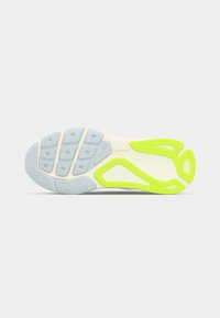 Semelle d'une chaussure de sport avec des motifs de bande de roulement gris et jaune néon sur fond blanc uni.