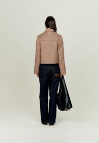 Pruun kareda mustriga jakk laiade varrukatega, tumedast denimist laiemad teksad ja must nahk kott. Teksapüksi taskul on nähtav brändi detail.