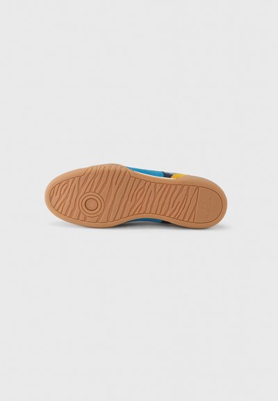 Σόλα πολύχρωμου αθλητικού παπουτσιού με ελαφρώς καφέ καουτσούκ πέλμα που διαθέτει κυκλικά και κυματιστά σχέδια, με το όνομα της μάρκας χαραγμένο κοντά στη φτέρνα.