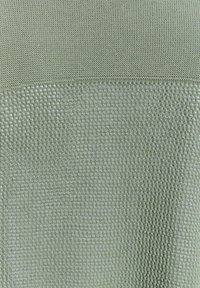 Gestructureerde groene stof met een mix van gebreide en geweven patronen, met een glad bovenstuk en een roosterachtig patroon eronder.