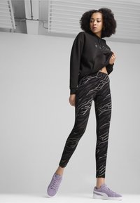 Zwarte cropped hoodie, aansluitende zwart-grijze leggings met zebra-print en paarse sneakers met witte zolen. Glad materiaal, stijlvol ontwerp.