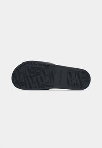 Semelle de chaussure noire avec motif géométrique de la bande de roulement et « Tommy Hilfiger » embossé au centre sur fond blanc.