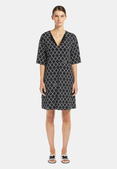 Abito nero con motivo geometrico bianco, scollatura a V, maniche corte e dettagli con bottoni sul davanti; abbinato a sandali piatti.