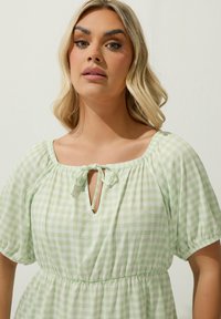 Vaaleanvihreä ruudullinen mekko, jossa on neliömäinen pääntie, solmikohta edessä, joustovyötärö ja lyhyet puffihelmaiset hihat. Pehmeä kangas.