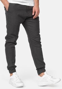 Pantalones jogger gris oscuro con puños elásticos, bolsillos frontales y un ajuste ceñido, combinados con zapatillas deportivas blancas. Textura suave, diseño casual.