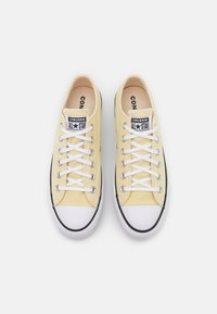 Baskets en toile jaune avec lacets blancs, accents noirs et embout en caoutchouc. Présente le logo "Converse All Star" sur la languette et le côté. Semelle plate.