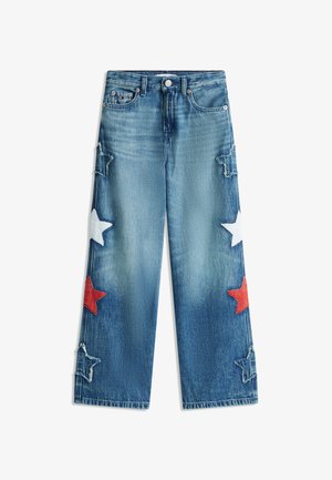 Jean en denim bleu à jambes larges, avec des patchs étoilés blancs, rouges et bleus effilochés sur les côtés.