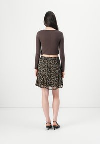 Brauner, langärmliger Cropped-Top, kombiniert mit einem schwarzen Blumenrock, der ein fließendes Design und transparente Textur aufweist. Getragen mit schwarzen High Heels.