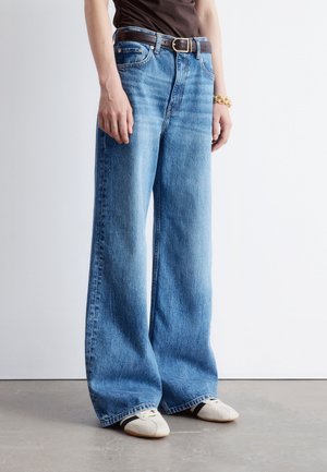 Wide-leg blue jeans with a high waist, made of denim, featuring a belt, sturdy seams, and a relaxed fit. Paired with light footwear.