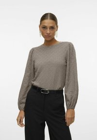 Blusa a maniche lunghe di un marrone chiaro texturizzato con scollo rotondo e maniche a sbuffo, abbinata a pantaloni neri a vita alta e una cintura nera sottile.