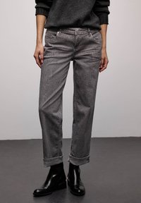 Grå mønstrede jeans med en let glans, med en klassisk pasform og opviklede manchetter, kombineret med ankelstøvler. Teksturen inkluderer et subtilt dyreprint.