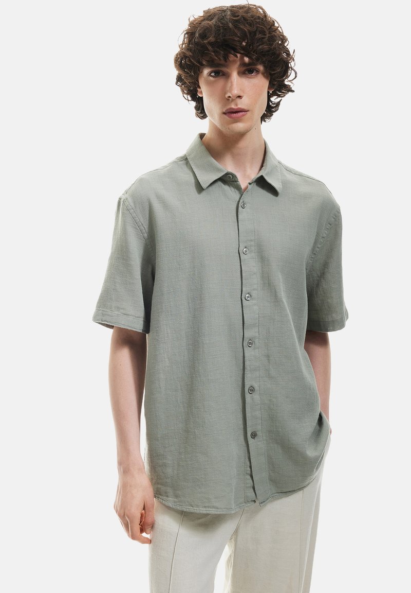 Korte mouw knoopshirt in lichtgroene stof, met een kraag, textuurafwerking en voorzakken. Simpele, losse pasvorm.