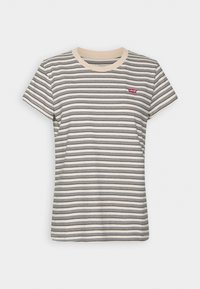Striped t-shirt in cream with black and navy stripes, featuring a round neckline and a small red branded label on the chest. Short sleeves.