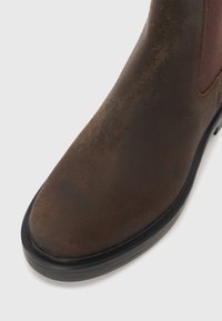 Botte Chelsea en cuir marron avec une finition lisse, des panneaux latéraux élastiques, un bout arrondi et une semelle en caoutchouc noir.