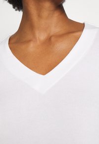 Top blanco de canalé con escote en V, que presenta un escote en forma de profunda V y una textura suave. La tela se estira ligeramente para mayor comodidad y ajuste.