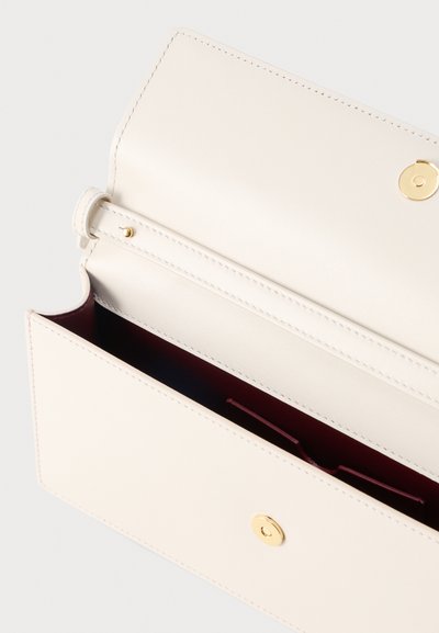 Εκρού δερμάτινο πορτοφόλι με χρυσό κουμπί κλεισίματος, ανοιχτό για να δείχνει την βαθιά βαθυκόκκινη εσωτερική επένδυση και τις ραμμένες άκρες.