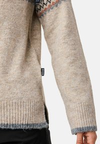 Beiger Strickpullover mit gemusterten Schulterakzenten in Blau und Rost. Verfügt über gerippte Bündchen und Saum, mit einem seitlichen Etikett, das "SEASIDE" trägt.