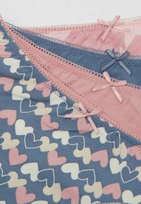 Tres pares de ropa interior en tonos azul claro, rosa y con un tejido estampado de corazones. Cada uno tiene un lazo decorativo y encaje en los bordes.