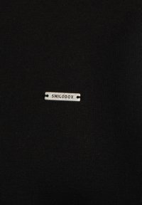 Tessuto nero con una superficie liscia, caratterizzato da un'etichetta metallica argentata con la scritta "SMILODOX" in lettere stampate e due piccoli fori.