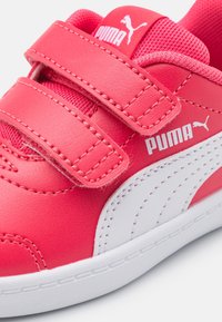 Zapatilla sintética rosa con dos correas ajustables de Velcro, logotipo de Puma blanco y suela de goma blanca. Presenta una textura suave y acentos en contraste.