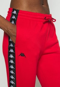 Rode sweatpants met een zwarte zijstreep en herhaalde witte logodesigns, elastische tailleband met trekkoord en zijzakken.