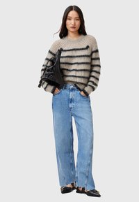 Beige gestreifter Pullover mit Rundhalsausschnitt, kombiniert mit hellblauen High-Waist-Jeans aus Denim. Eine schwarze glänzende Handtasche und spitze Ballerinas runden das Outfit ab.